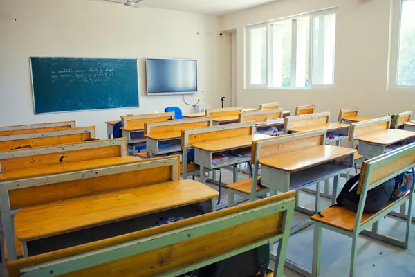 Rows of wooden desks and chairs in an empty classroom