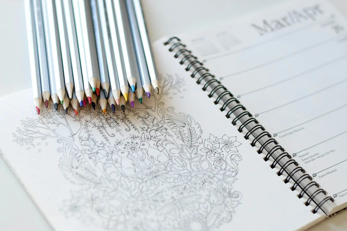 Coloured pencils resting on an illustrated colouring notebook